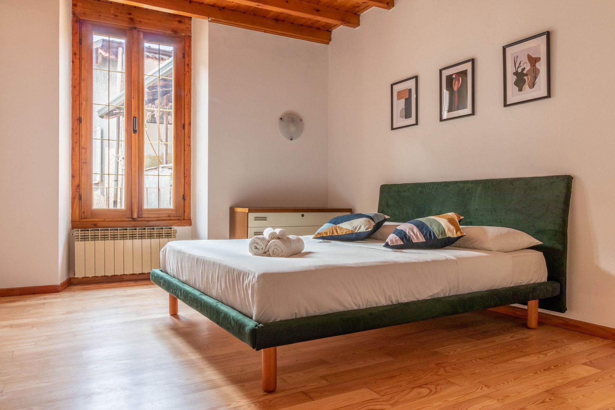 Guest bedroom with green bed, tall window, and framed artwork