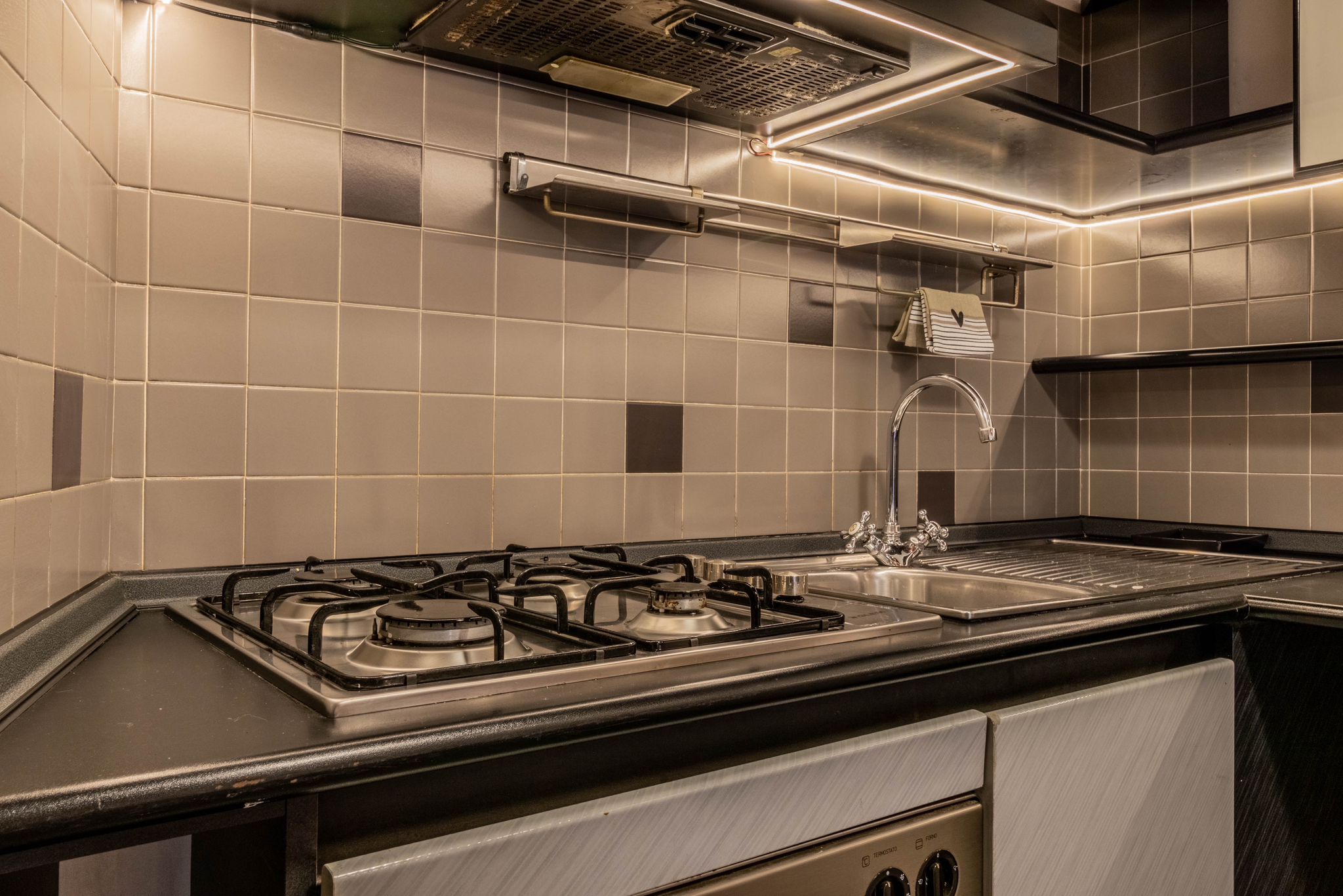 Gas hob and sink in the kitchen with tiled backsplash and task lighting
