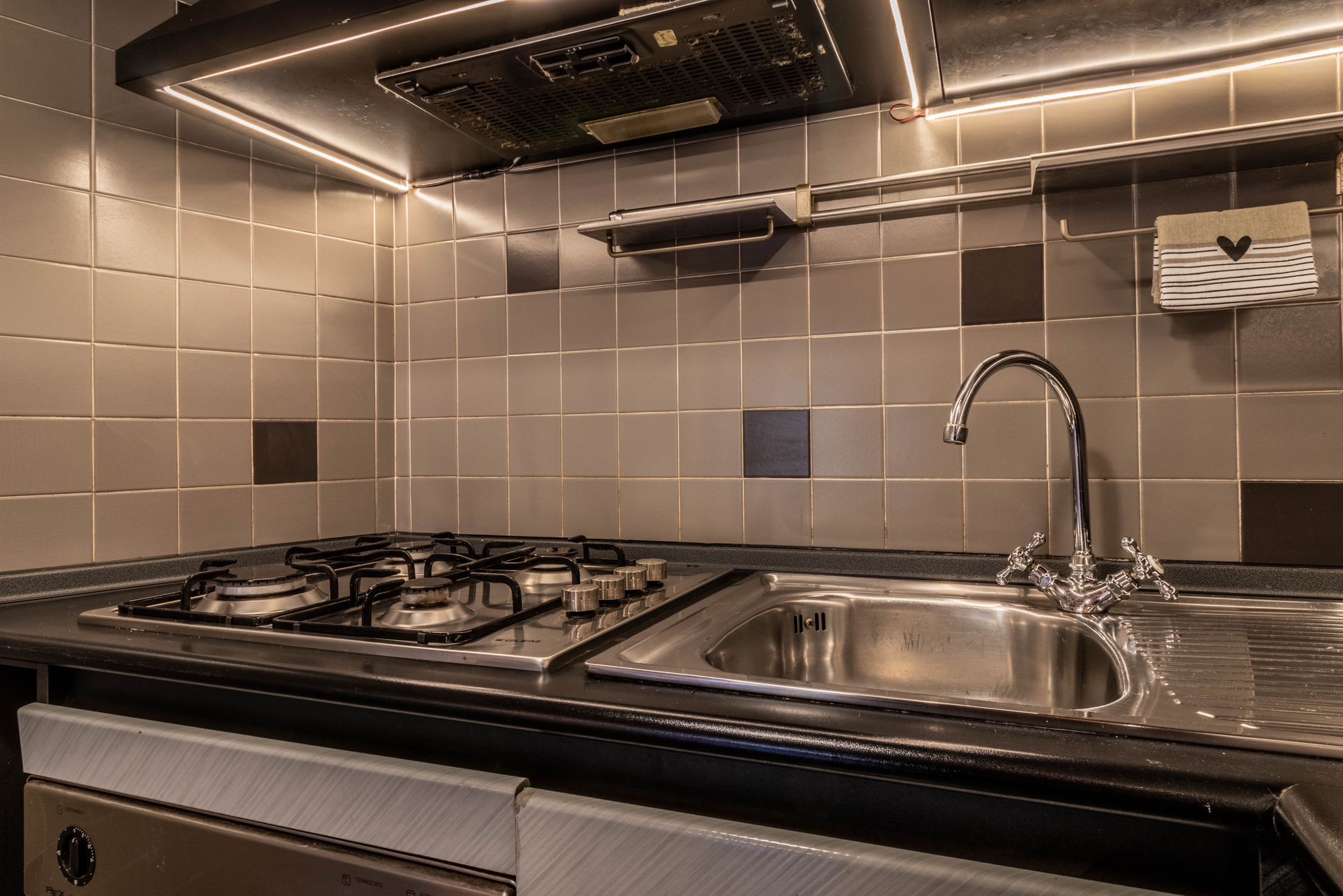 Kitchen sink and gas hob with tiled backsplash and under-cabinet lighting
