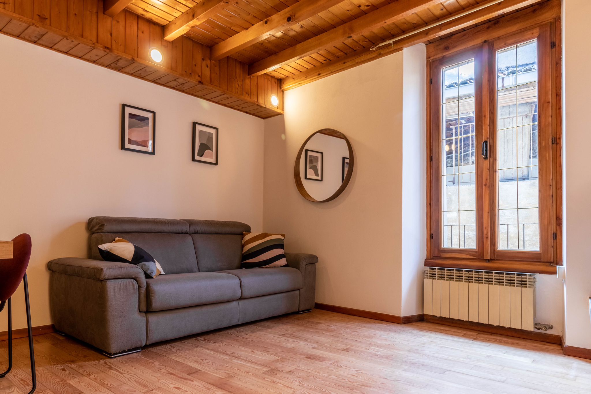 Living area sofa beside a tall window and round mirror