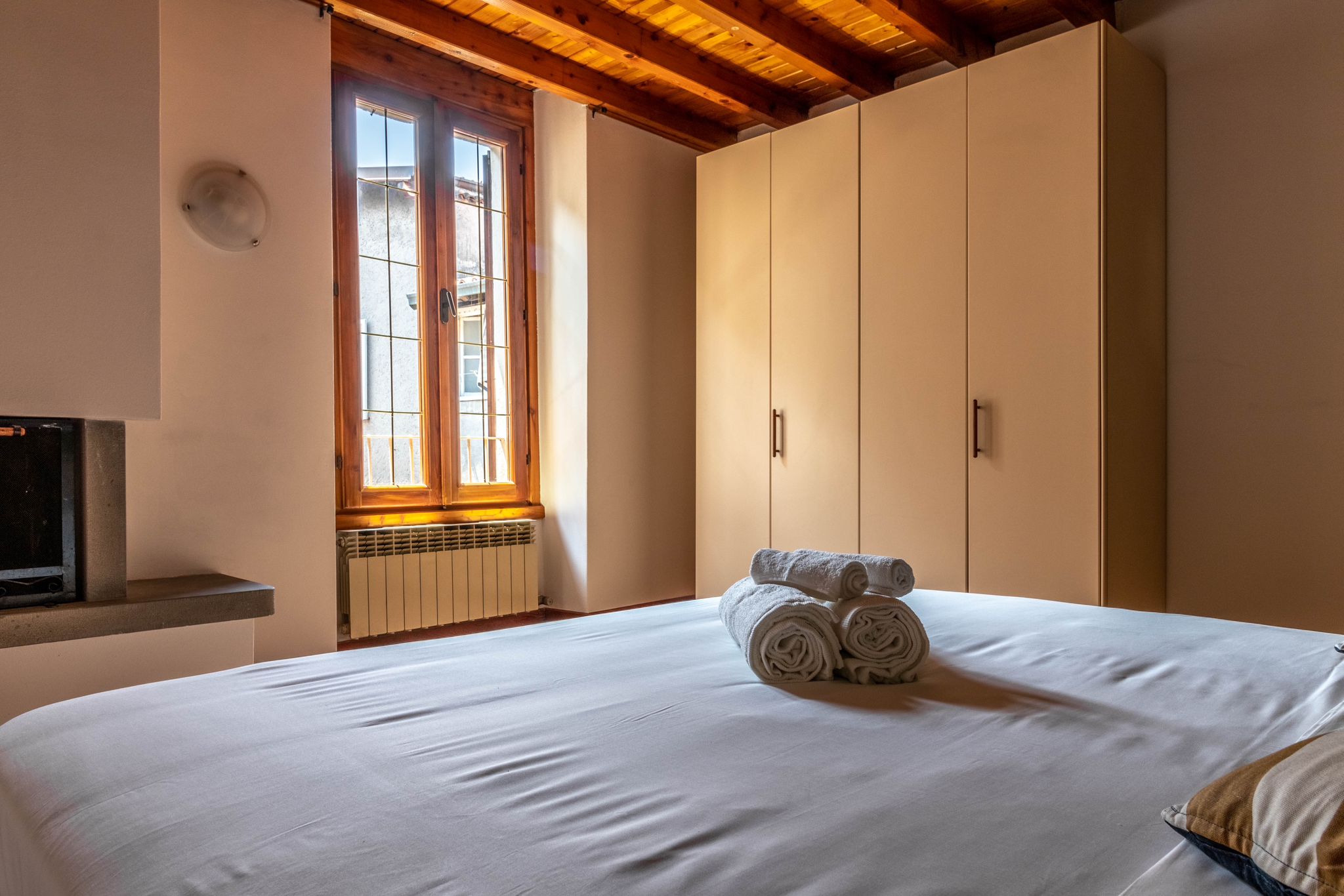 Primary bedroom with wardrobe, tall window, and folded towels on the bed